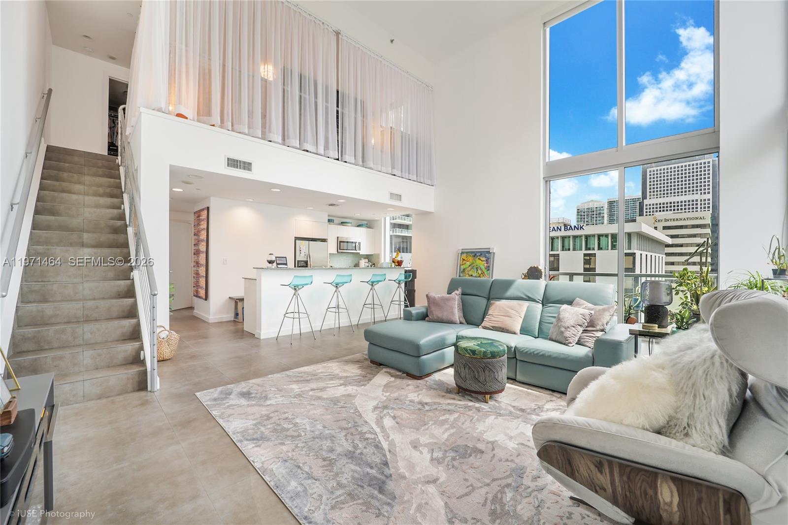 A modern living room with high ceilings, a staircase, a kitchen, and floor-to-ceiling windows — 1060 Brickell Ave # 1003, Miami FL 33131, MIAMI, FL