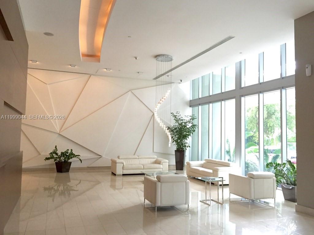 A modern lobby features white leather furniture, geometric wall panels, and floor-to-ceiling windows — 79 SW 12th St, Miami FL 33130, MIAMI, FL