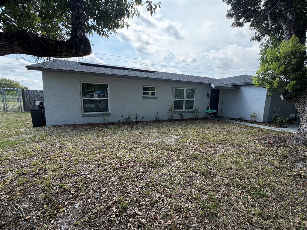 A single-story house with a gray stucco exterior, a shingled roof, and a leaf-covered yard — 4614 LEMANS DRIVE, ORLANDO, FL