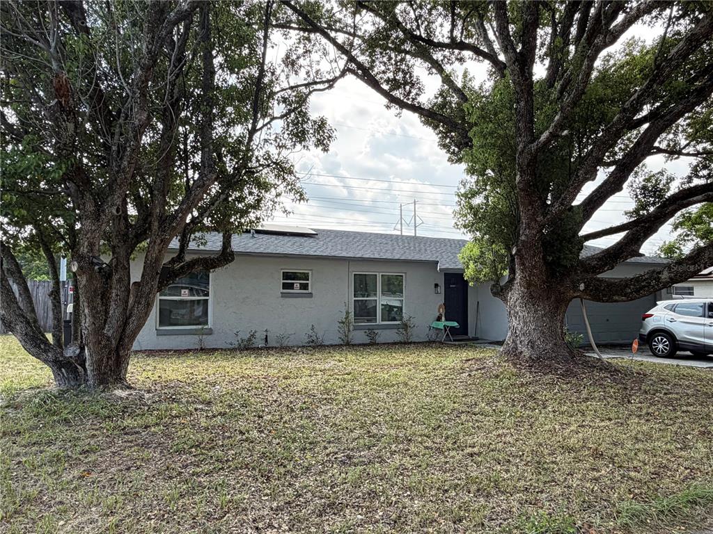 A single-story house with a gray exterior, two large trees, and a driveway with a car — 4614 LEMANS DRIVE, ORLANDO, FL
