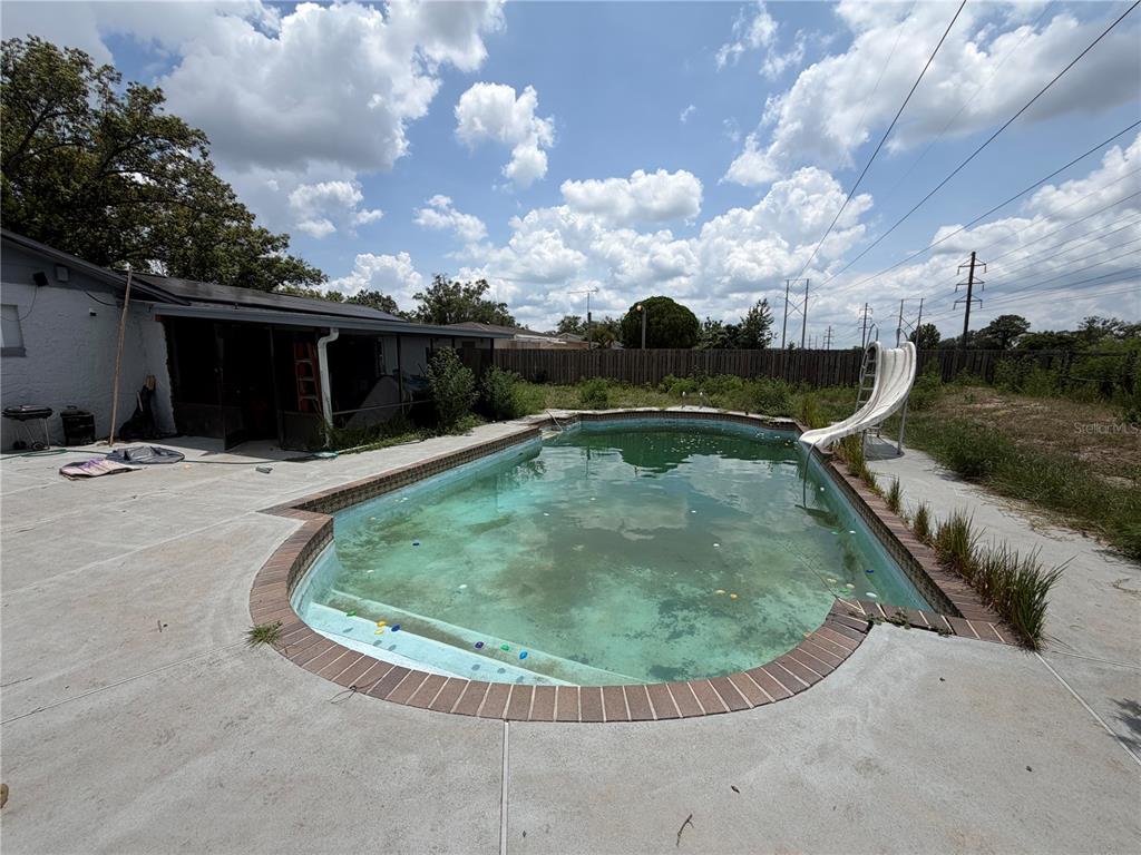 A backyard features a concrete patio, an in-ground swimming pool with a slide, and overgrown landscaping — 4614 LEMANS DRIVE, ORLANDO, FL