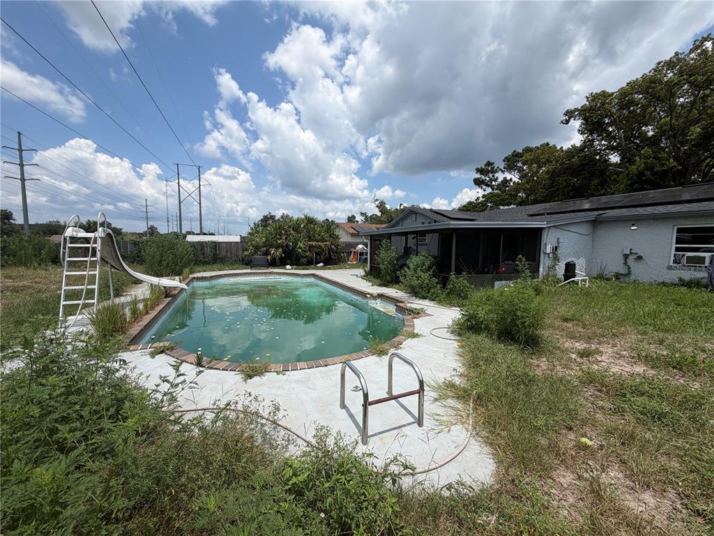 A backyard features an overgrown lawn, a swimming pool with a slide, and a house — 4614 LEMANS DRIVE, ORLANDO, FL