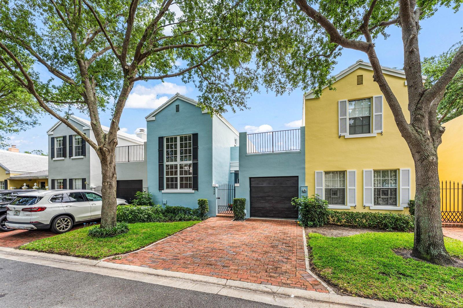 A row of colorful townhouses with brick driveways, garages, and mature trees in front — 5908 Catesby Street, Boca Raton FL 33433, BOCA RATON, FL