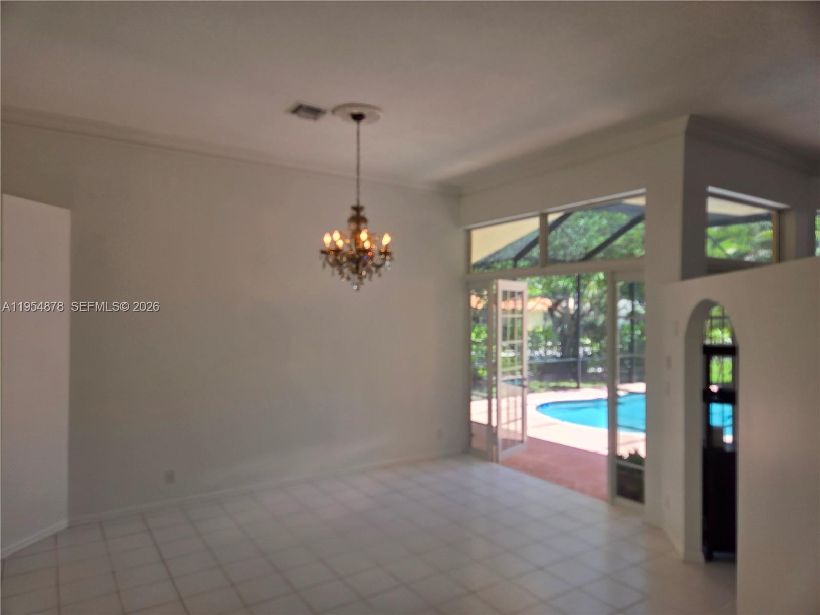A bright living room with white tile floors, a chandelier, and sliding doors to a pool — 900 Spoonbill Cir, Weston FL 33326, WESTON, FL