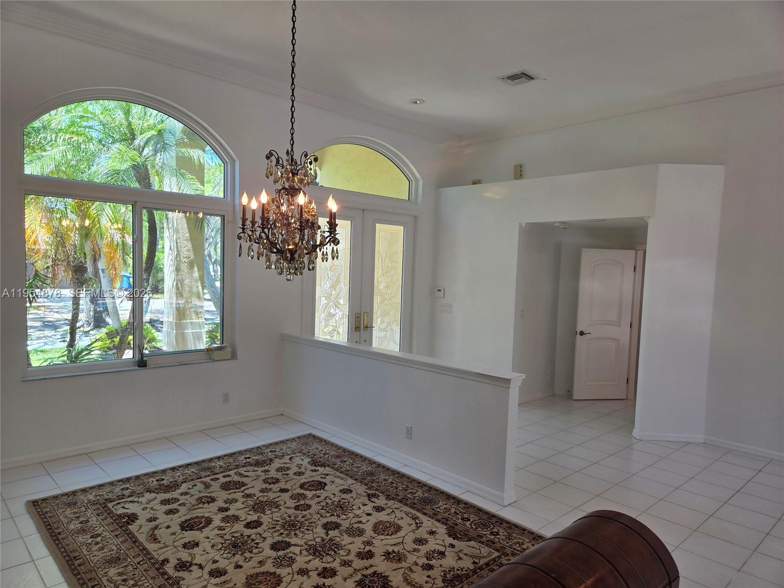 A bright room features a crystal chandelier, large arched windows, and a patterned area rug — 900 Spoonbill Cir, Weston FL 33326, WESTON, FL