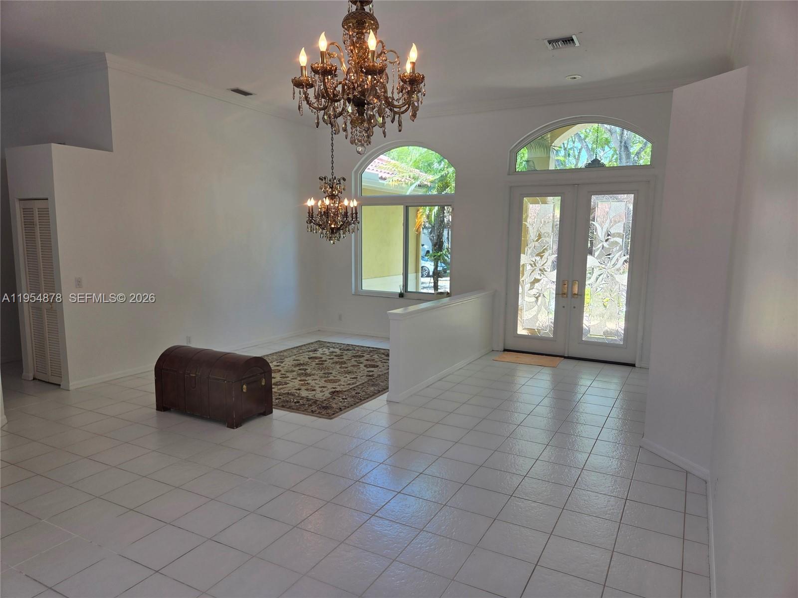 A bright foyer features white tile floors, two ornate chandeliers, and a decorative wooden chest — 900 Spoonbill Cir, Weston FL 33326, WESTON, FL