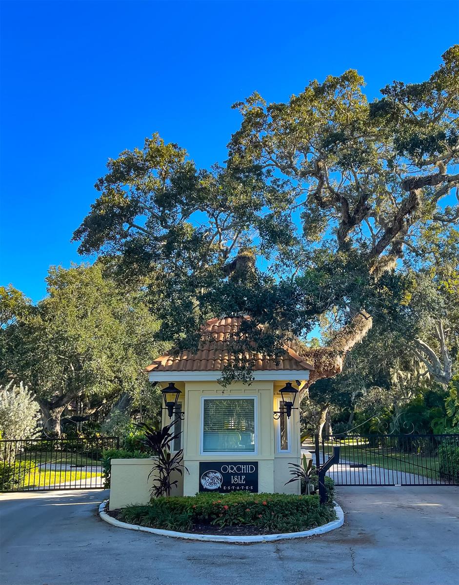 A gated entrance features a small guardhouse with a tiled roof under large oak trees — 2545 Riverview Court, Vero Beach FL 32963, VERO BEACH, FL