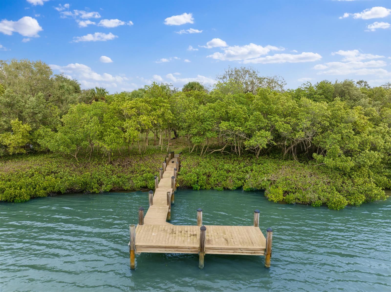 An aerial view of a wooden dock extending from a lush, tree-lined shoreline into water — 2545 Riverview Court, Vero Beach FL 32963, VERO BEACH, FL