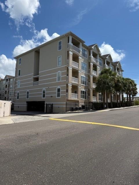 A multi-story apartment building with balconies and palm trees stands beside a paved road — 1216 S MISSOURI AVENUE UNIT 227, CLEARWATER, FL
