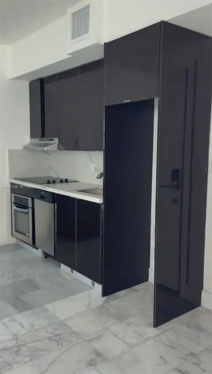 A modern kitchen features glossy black cabinetry, stainless steel appliances, and white marble flooring — 1560 Drexel Ave # 103, Miami Beach FL 33139, MIAMI BEACH, FL