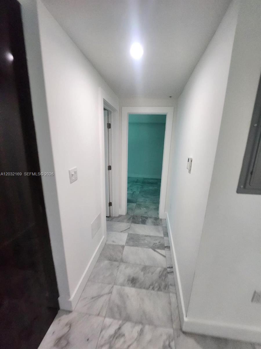 A hallway with white walls and gray marble tile flooring leads to an open doorway — 1560 Drexel Ave # 103, Miami Beach FL 33139, MIAMI BEACH, FL