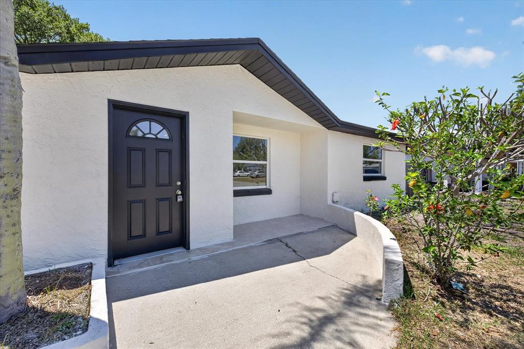 A white house exterior features a dark front door, a concrete walkway, and a curved wall — 3851 SATURN DRIVE, NEW PORT RICHEY, FL