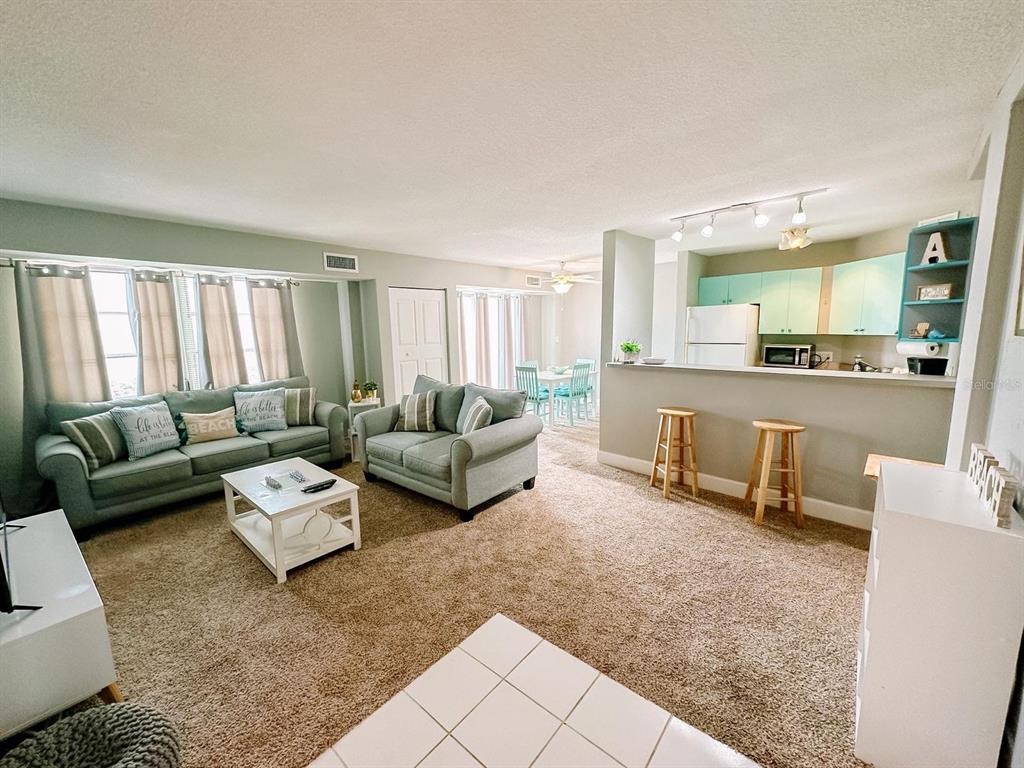 A living room with beige carpet, light blue sofas, and an open kitchen with bar stools — 3315 58TH AVENUE S UNIT 414, ST PETERSBURG, FL