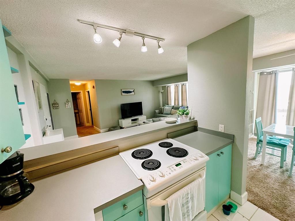 A kitchen with teal cabinets and a white stove overlooks a living room and dining area — 3315 58TH AVENUE S UNIT 414, ST PETERSBURG, FL