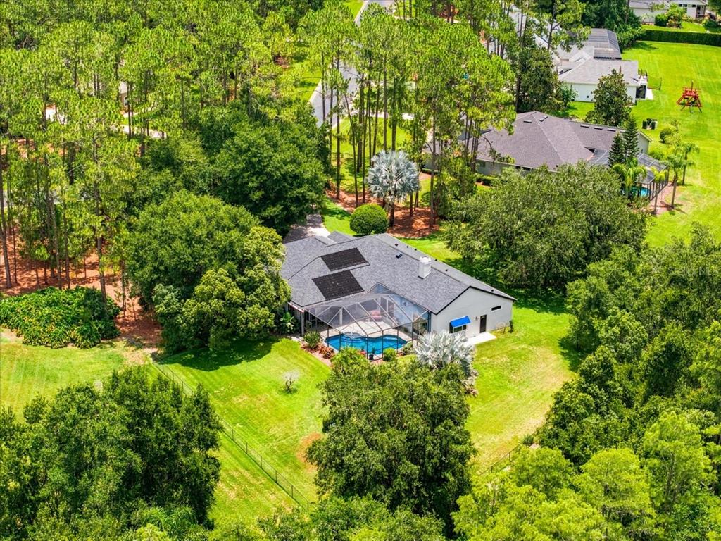 An aerial view shows a house with a pool, screened lanai, and solar panels — 418 PINE BLUFF DRIVE, LUTZ, FL