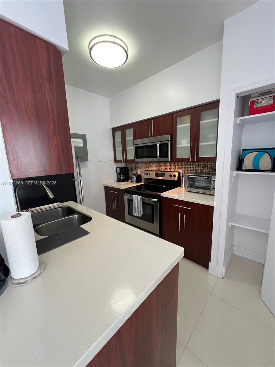 A kitchen features dark wood cabinets, stainless steel appliances, and a light-colored countertop — 1100 Collins Ave # 303, Miami Beach FL 33139, MIAMI BEACH, FL