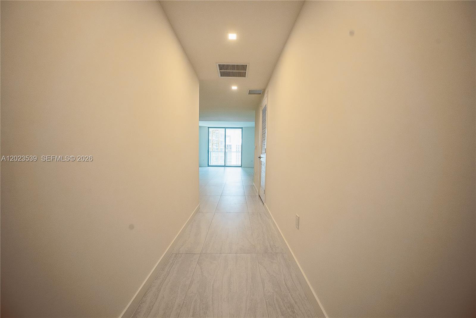 A long, narrow hallway with light-colored tile flooring leads toward a bright windowed room — 77 SE 5th St # 2203, Miami FL 33131, MIAMI, FL
