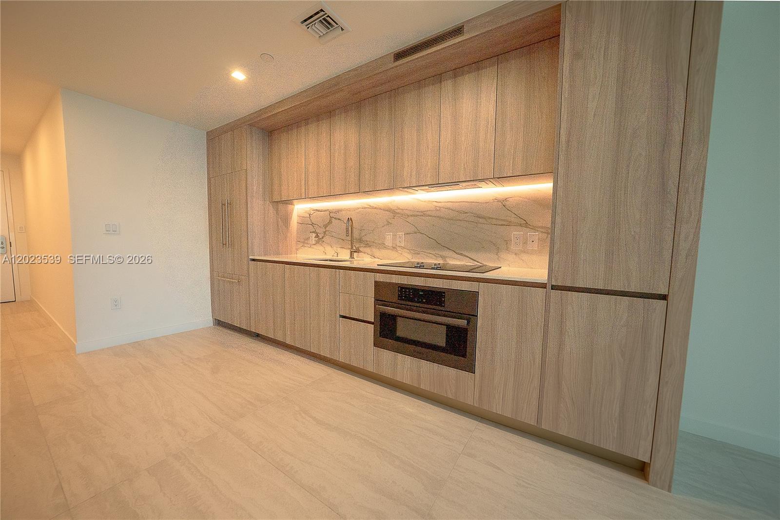 A modern kitchen features light wood cabinetry, a marble backsplash, and integrated stainless steel appliances — 77 SE 5th St # 2203, Miami FL 33131, MIAMI, FL