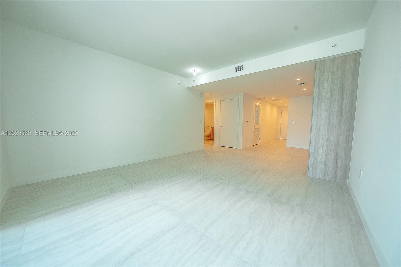 An empty room features light-colored tile flooring, white walls, and a wood-paneled accent wall — 77 SE 5th St # 2203, Miami FL 33131, MIAMI, FL