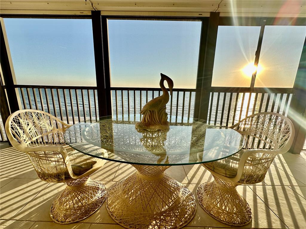 A glass-topped table and two wicker chairs sit on a screened balcony overlooking the ocean — 15462 GULF BOULEVARD UNIT 501, MADEIRA BEACH, FL