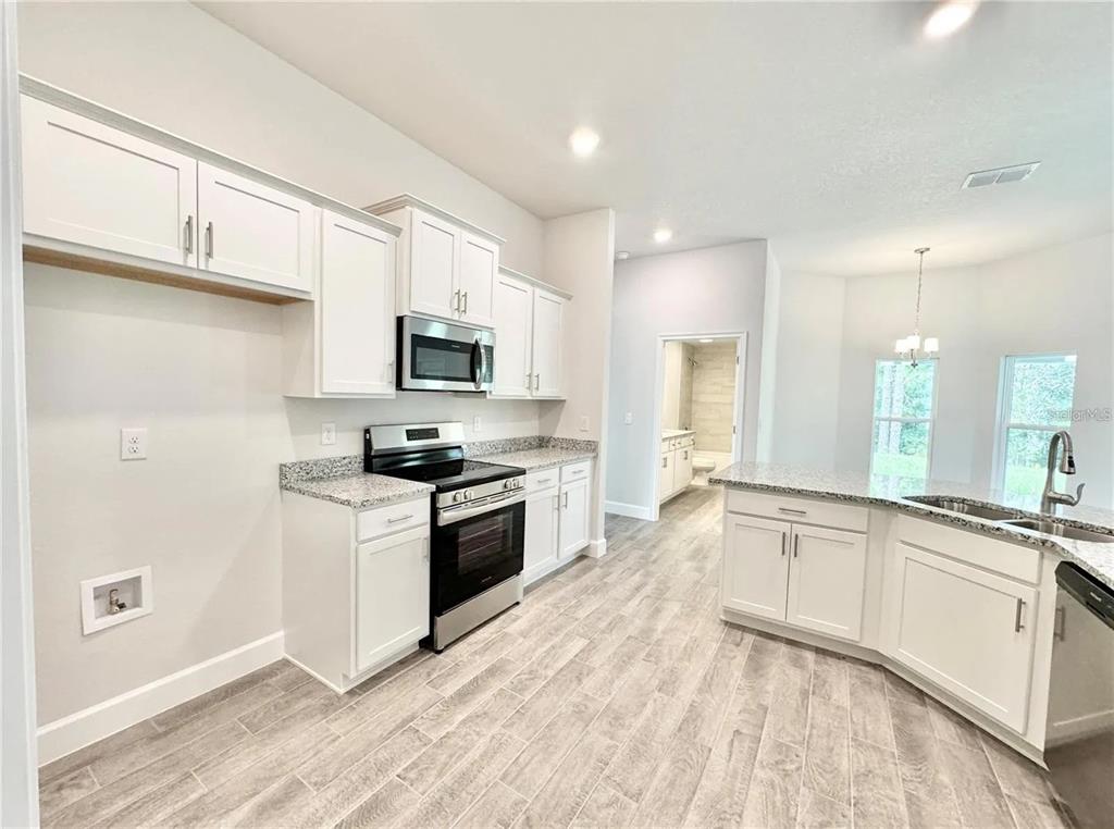 A kitchen features white cabinets, granite countertops, stainless steel appliances, and light wood-look flooring — 17745 SW 72ND STREET ROAD, DUNNELLON, FL