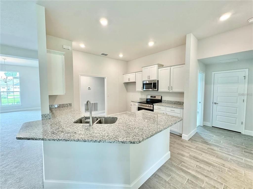 A kitchen with white cabinets, granite countertops, and a peninsula sink overlooking a carpeted room — 17745 SW 72ND STREET ROAD, DUNNELLON, FL