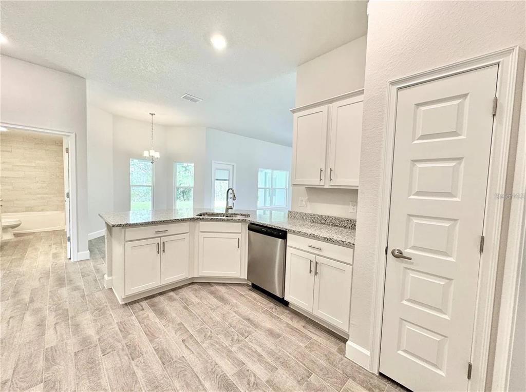 A kitchen features white cabinets, granite countertops, stainless steel appliances, and wood-look tile flooring — 17745 SW 72ND STREET ROAD, DUNNELLON, FL