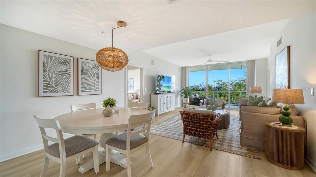 A bright, open-concept living and dining area features light wood flooring and a balcony view — 1800 BENJAMIN FRANKLIN DRIVE UNIT B308, SARASOTA, FL