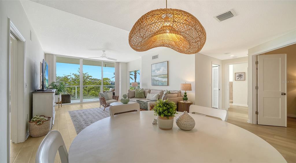 A bright living and dining area features light wood floors, a woven pendant light, and balcony — 1800 BENJAMIN FRANKLIN DRIVE UNIT B308, SARASOTA, FL