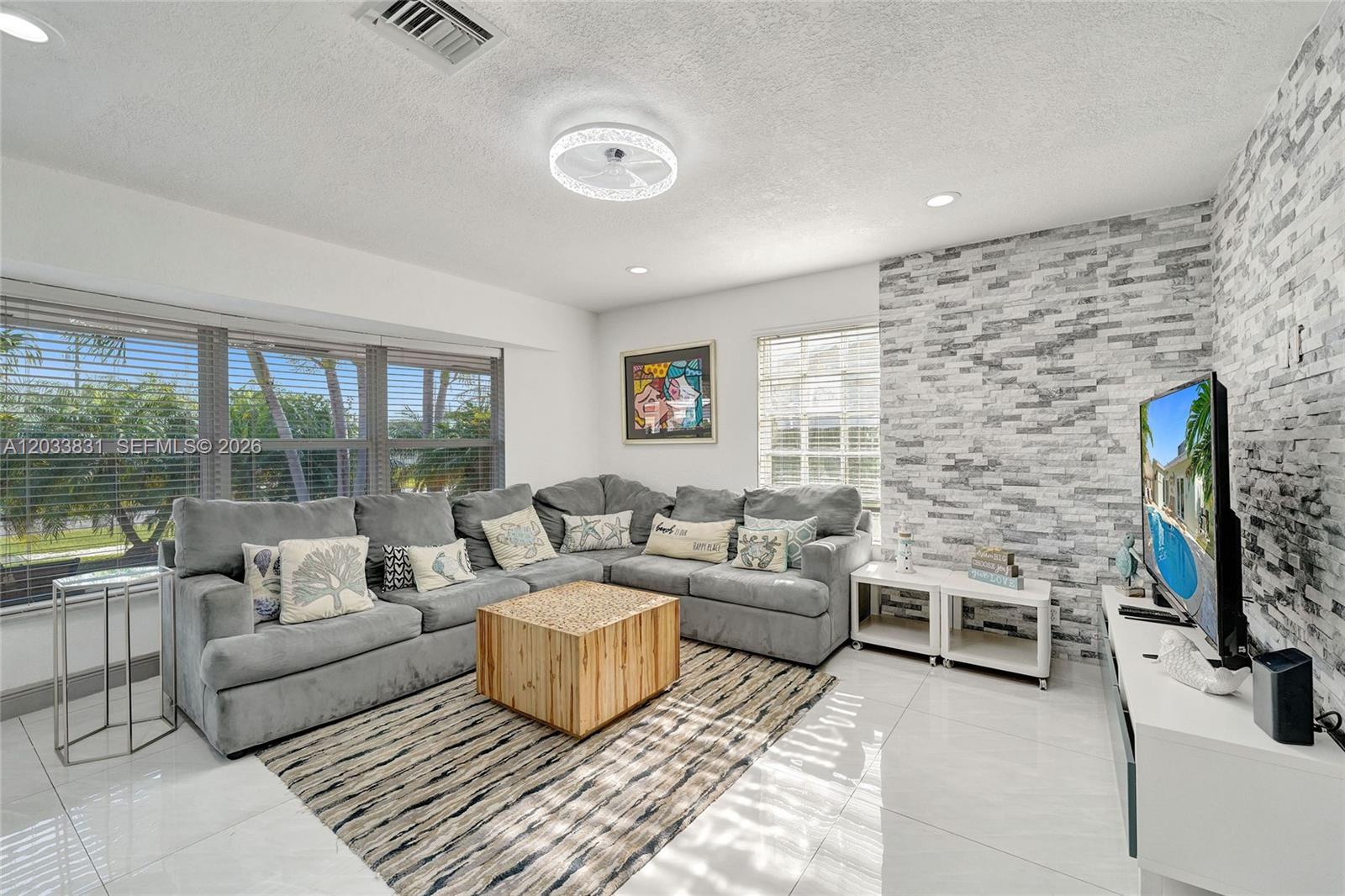 A living room features a gray sectional sofa, a wooden coffee table, and a stone wall — 218 SE 4th st # 0, Dania Beach FL 33004, DANIA BEACH, FL
