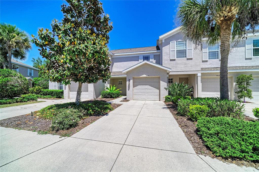 A two-story townhouse with a beige stucco exterior, a single-car garage, and a concrete driveway — 14830 SKIP JACK LOOP, LAKEWOOD RANCH, FL