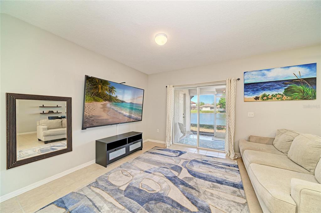 A living room features a large television, a patterned rug, and sliding doors to a patio — 14830 SKIP JACK LOOP, LAKEWOOD RANCH, FL