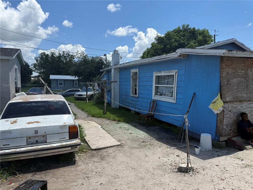 A blue house with a plywood-covered wall sits next to a white car — 810 PERSON STREET, KISSIMMEE, FL