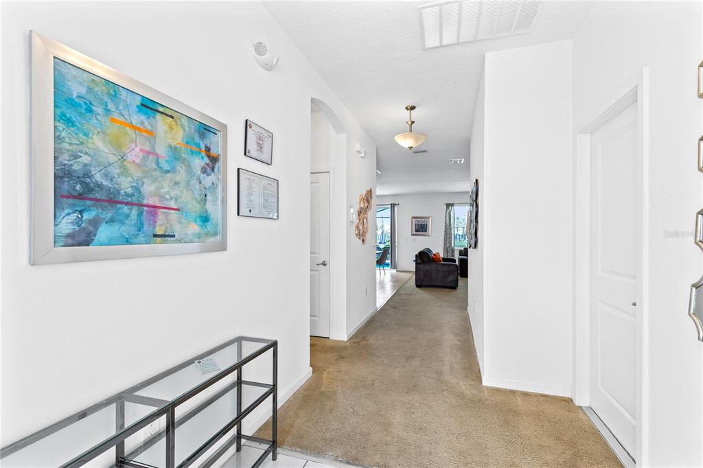 A carpeted hallway leads from a tiled entryway toward a living area with a sofa — 320 BALLO DRIVE, KISSIMMEE, FL
