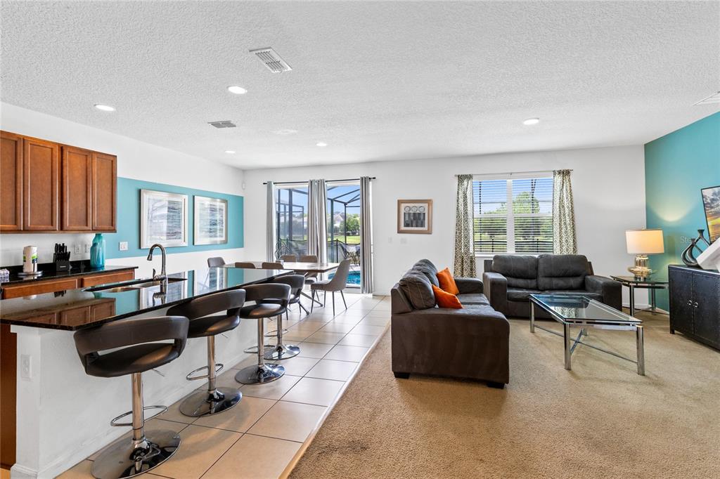 An open-concept kitchen and living room with tile flooring, a breakfast bar, and pool access — 320 BALLO DRIVE, KISSIMMEE, FL