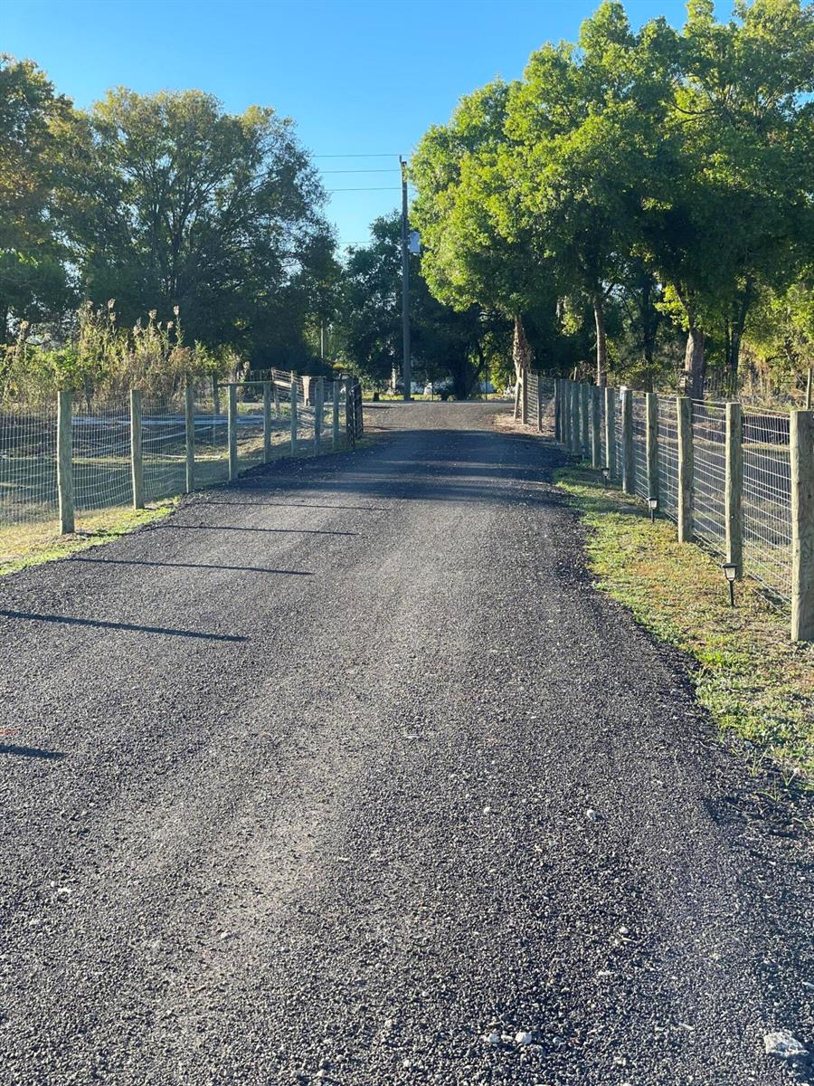 A gravel driveway leads toward a gate between two fenced areas lined with trees — 1220 A Road, FL 33935, FL