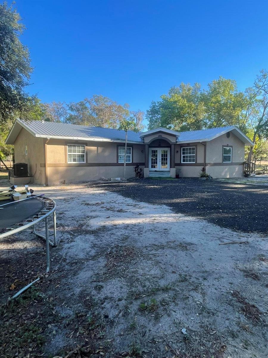 A single-story house with a metal roof, stucco exterior, and a large gravel driveway — 1220 A Road, FL 33935, FL