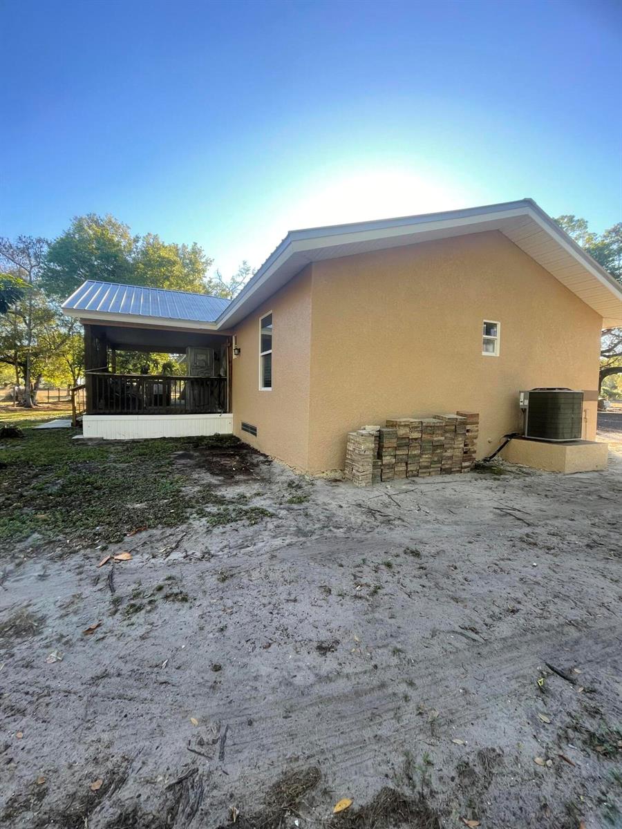 A tan stucco house exterior features a covered porch with a metal roof and HVAC unit — 1220 A Road, FL 33935, FL