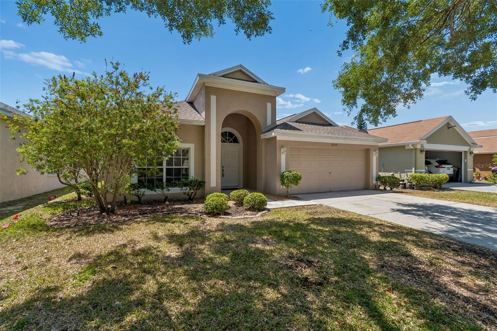 A tan single-story house with a two-car garage and a prominent arched entryway — 4789 WHISPERING WIND AVENUE, TAMPA, FL
