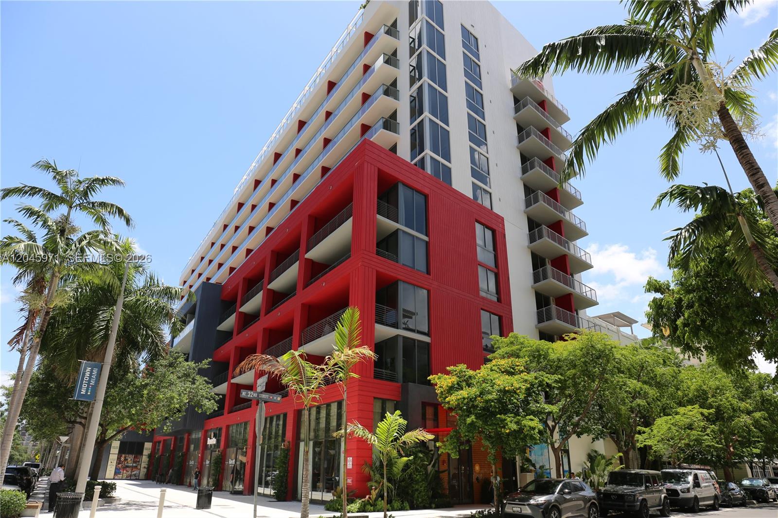 A multi-story building features a prominent red facade, glass balconies, and surrounding palm trees — 90 NE 32nd St # 702, Miami FL 33137, MIAMI, FL