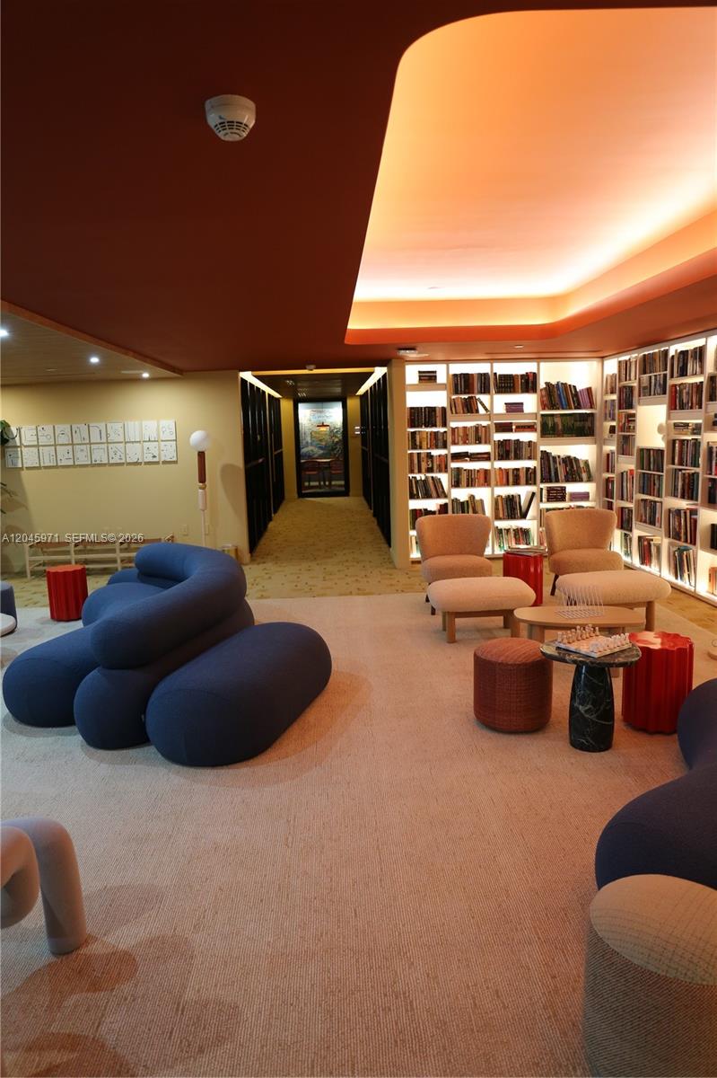 A lounge area features a blue sculptural sofa, armchairs, bookshelves, and a long hallway — 90 NE 32nd St # 702, Miami FL 33137, MIAMI, FL