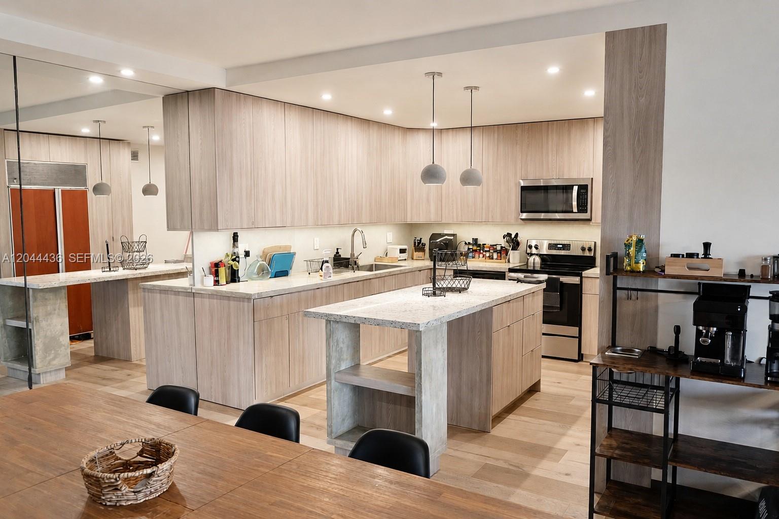 A modern kitchen features light wood cabinetry, a central island, and stainless steel appliances — 770 NE 199th St # 107F, Miami FL 33179, MIAMI, FL