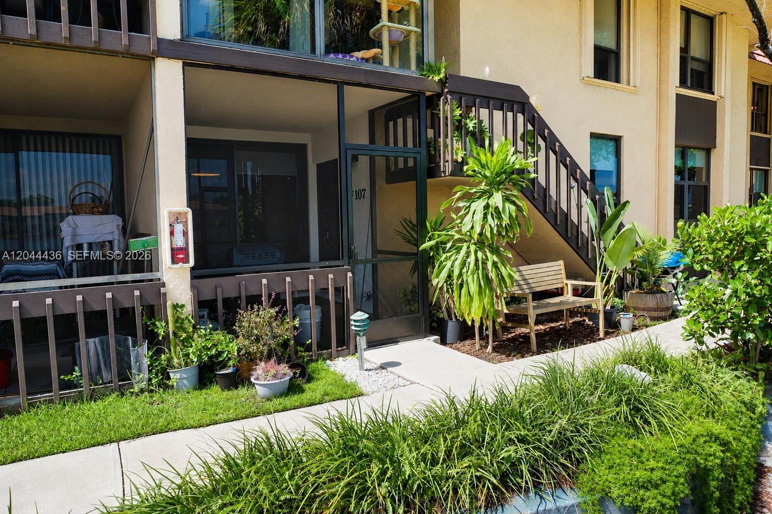 A ground-floor apartment entrance features a screened patio, a wooden bench, and exterior stairs — 770 NE 199th St # 107F, Miami FL 33179, MIAMI, FL
