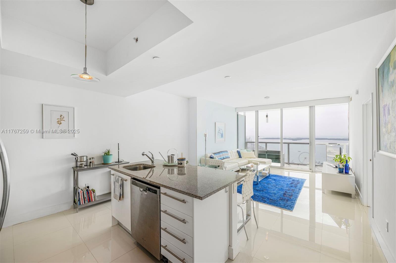 A modern kitchen island with granite countertops overlooks a living area with a balcony view — 888 Biscayne Blvd # 4306, Miami FL 33132, MIAMI, FL