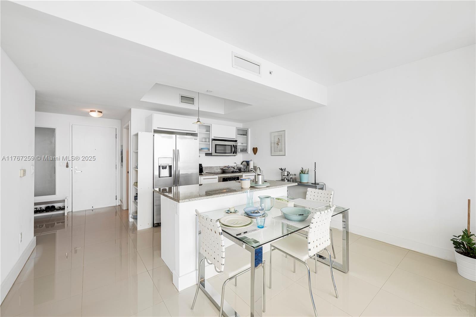 A modern kitchen features white cabinetry, granite countertops, and a glass-topped dining table — 888 Biscayne Blvd # 4306, Miami FL 33132, MIAMI, FL
