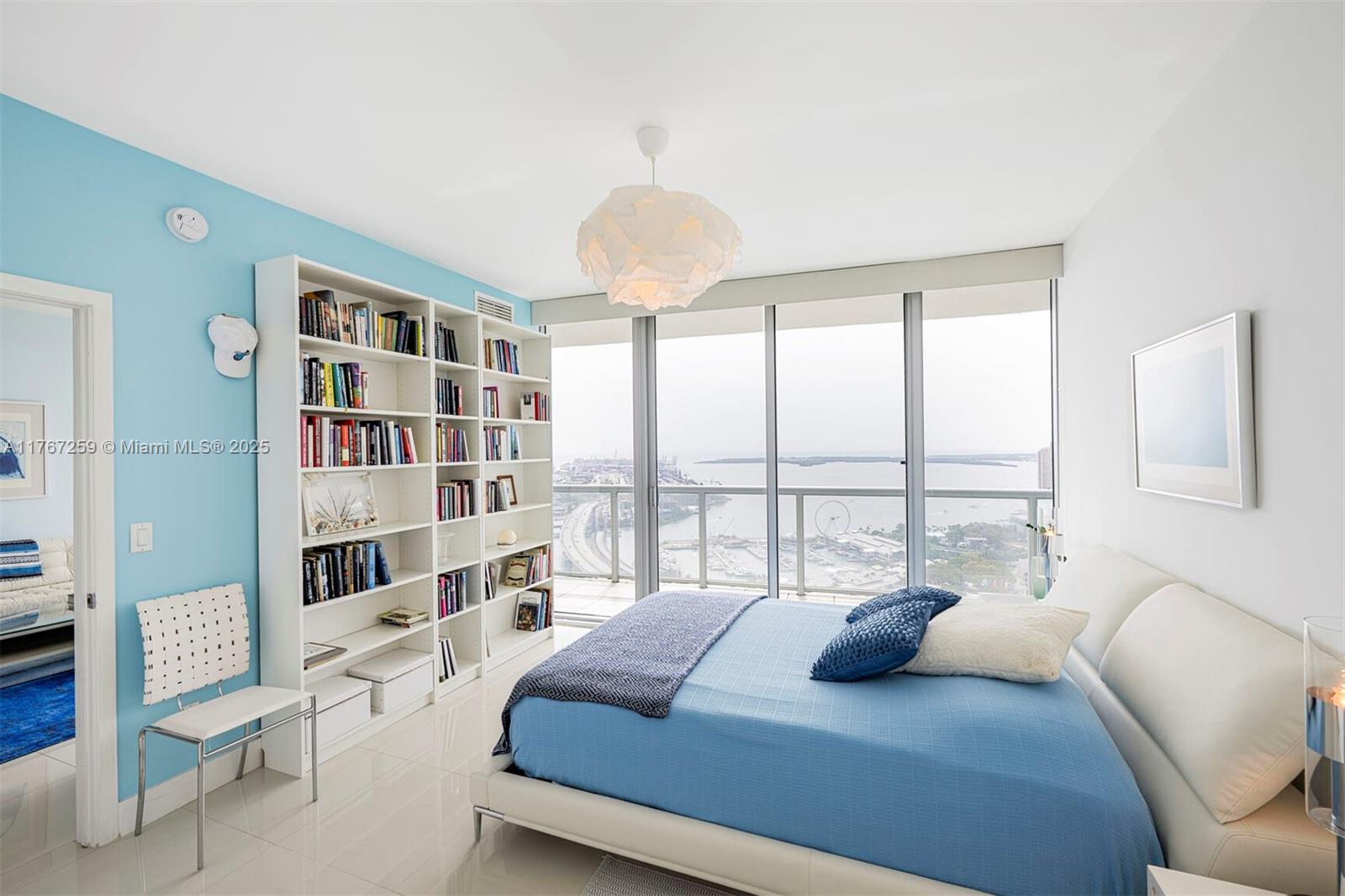 A bedroom with a blue accent wall, white bookshelf, and floor-to-ceiling windows overlooking the water — 888 Biscayne Blvd # 4306, Miami FL 33132, MIAMI, FL