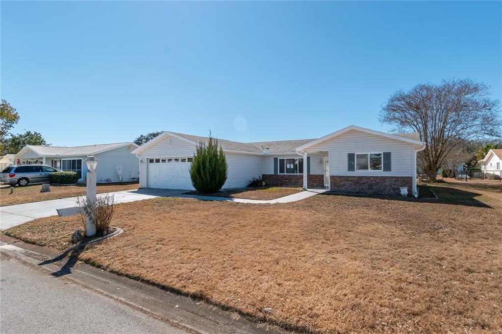 A single-story house with light gray siding, a brick base, and a white garage door — 17952 SE 107TH COURT, SUMMERFIELD, FL