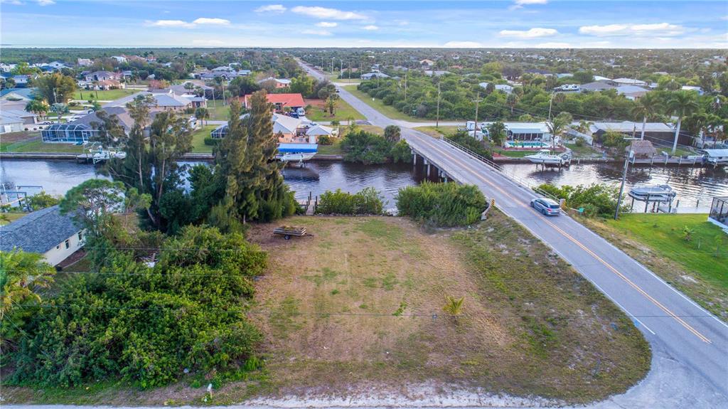 An aerial view shows a vacant waterfront lot next to a road and a bridge — 19379 MIDWAY BOULEVARD, PORT CHARLOTTE, FL
