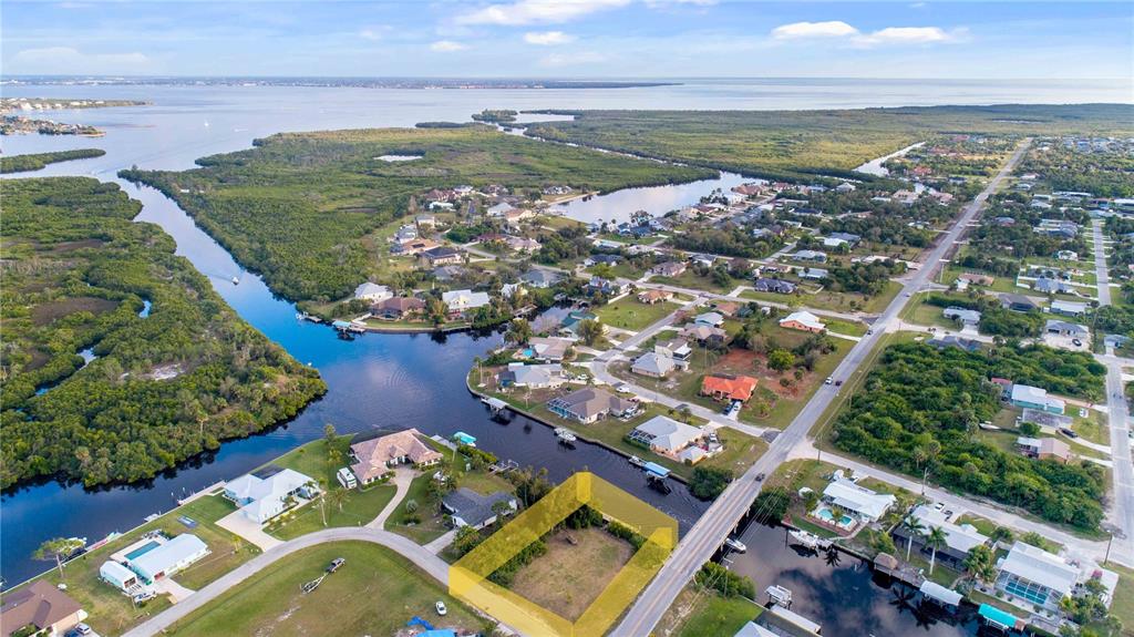 An aerial view shows a vacant waterfront lot highlighted in yellow next to a road — 19379 MIDWAY BOULEVARD, PORT CHARLOTTE, FL