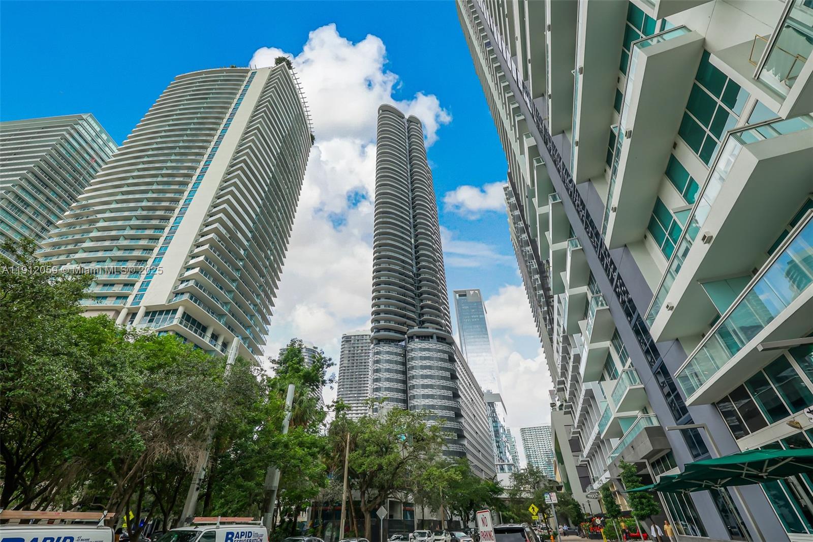 A low-angle view shows several modern high-rise apartment buildings against a blue sky — 1000 Brickell Plz # 3002, Miami FL 33131, MIAMI, FL